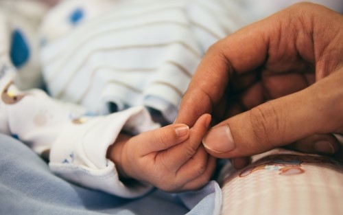 A newborn hand holding an adults hand.