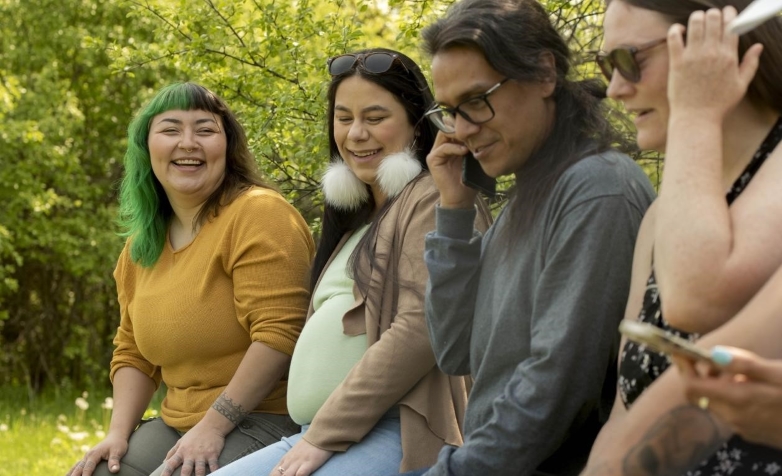 Four Indigenous adults, representing a range of genders, sitting together and laughing.