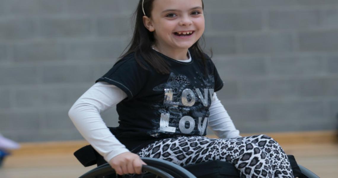 A school-aged girl smiling in a wheelchair.