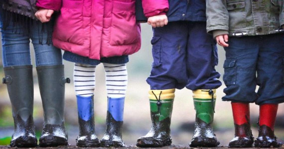 Four children, representing a mix of genders, standing with multi-coloured rainboots.
