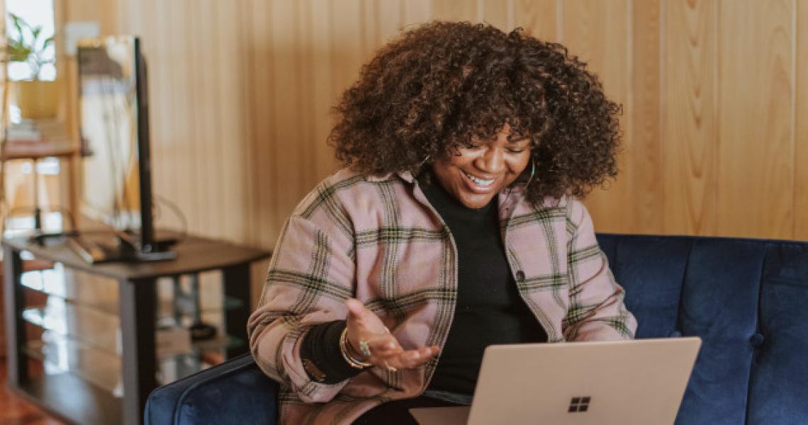 A Black woman with curly hair smiling and looking at her laptop.