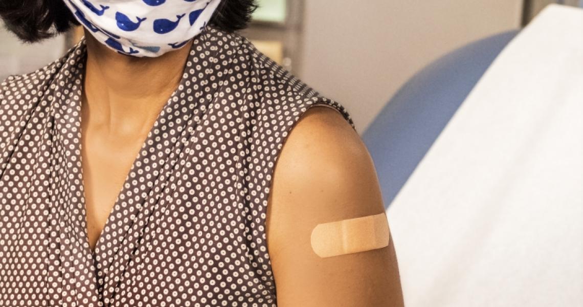 A Brown woman wearing a mask with blue whales on it sitting with a band aid on her arm after receiving a vaccine.