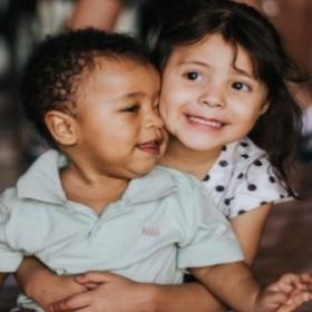 Two young children of mixed races and genders, hugging and smiling.