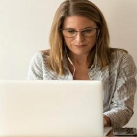 A white woman wearing earphones working on a laptop.