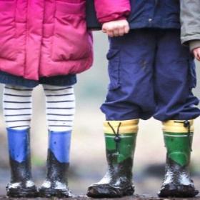 Two children, representing a mix of genders, standing with multi-coloured rainboots.
