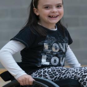 A school-aged girl smiling in a wheelchair.