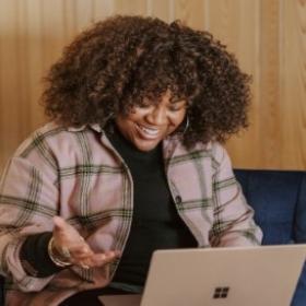 Black woman with curly hair smiling at her laptop.