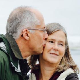 An elderly white man kissing the cheeck of an elderly white woman.