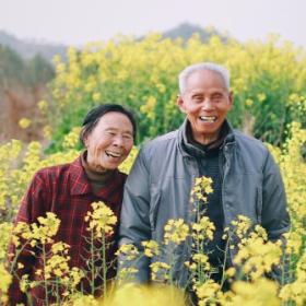 Two East Asian elderly adults smiling in a field.
